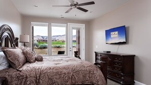 Ein Schlafzimmer mit einem großen Bett, einer Kommode, einem Fernseher und Blick auf eine gebirgige Landschaft durch die Tür.