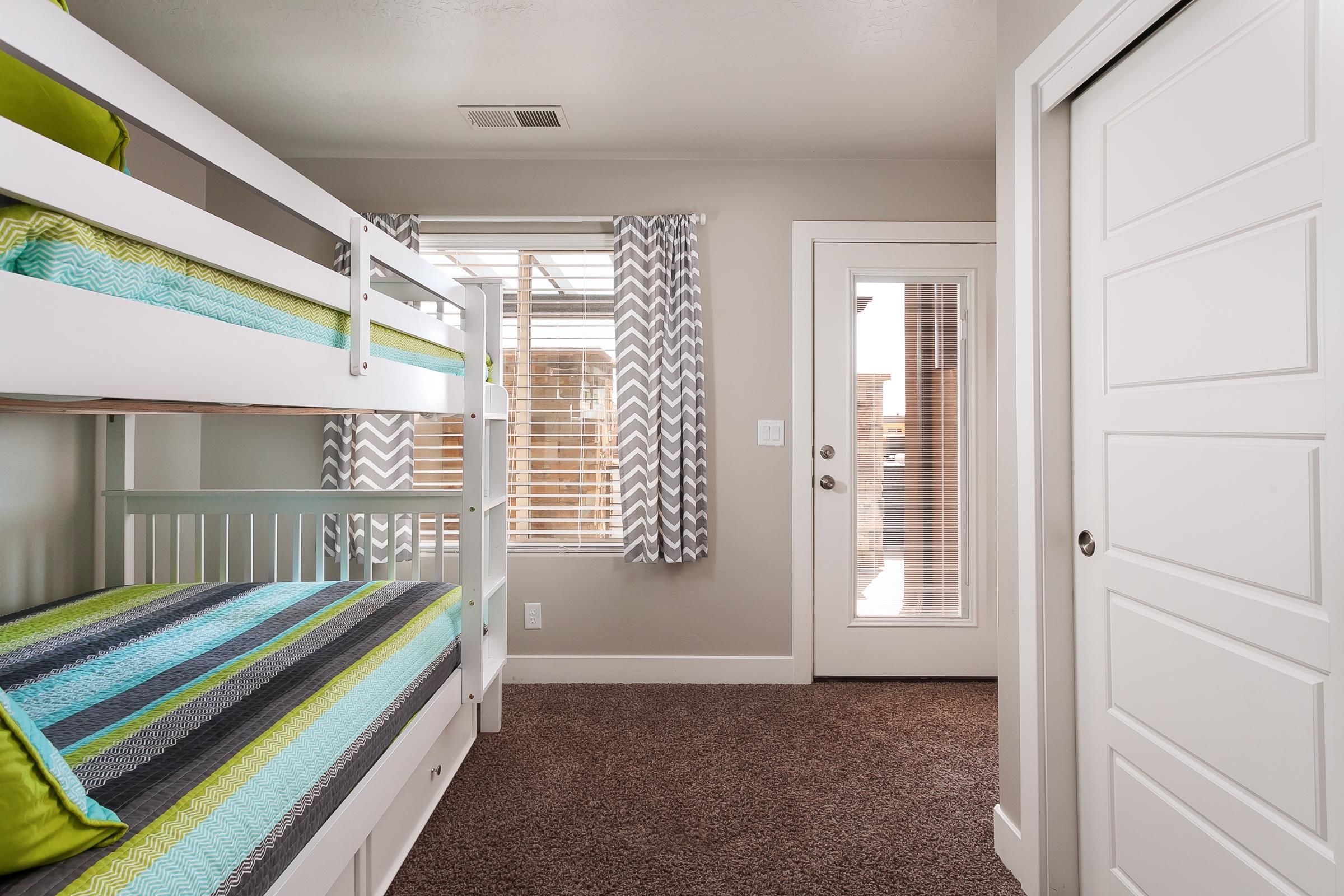 A room with bunk beds, a door, and a window with curtains.