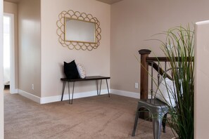 A room with a beige carpet, a bench with a mirror, a potted plant, and a staircase. - The Perfect Place (St. George)