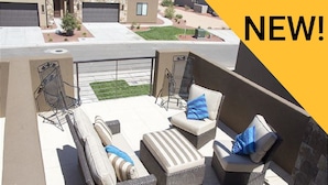 A balcony with wicker furniture, including a sofa, two armchairs, and a small ottoman, with a view of a residential street. - The Perfect Place (St. George)