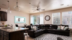 A modern living room with a dark leather sectional sofa, a kitchen island, and a ceiling fan. - The Perfect Place (St. George)