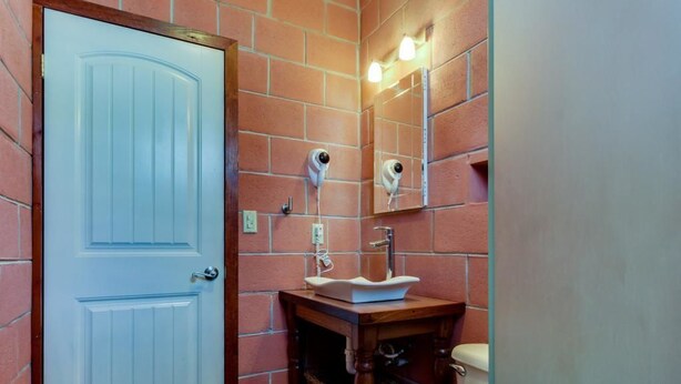 A bathroom with a white door, a wooden vanity with a sink, a toilet, and a mirror with lights. - Casa Zazil Ha (Belmopan)
