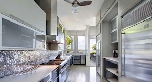 A modern kitchen with a stone backsplash, stainless steel appliances, and a view of the outdoors. - Villa Angela (Miami Beach)