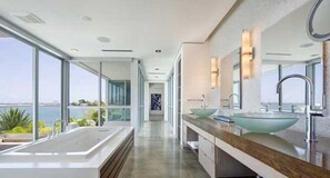 A modern bathroom with large windows, a long vanity, and a bathtub.