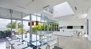 A modern hotel room with a large glass window, a white sofa, and a dining area with a glass table. - Villa Angela (Miami Beach)