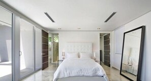 A modern bedroom with a large bed, built-in wardrobe, and sliding glass doors leading to a balcony.