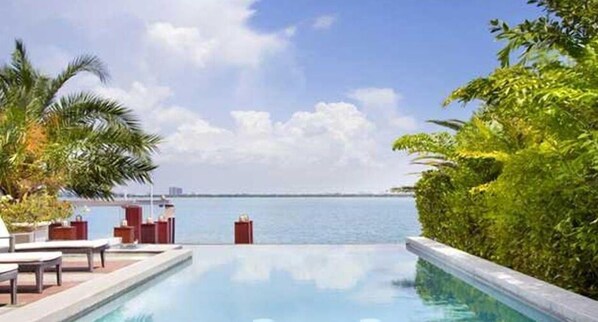 A pool area with lounge chairs and a view of the sea.