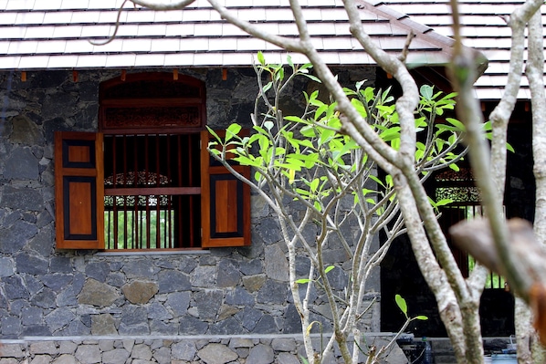 A stone building with a window featuring wooden shutters and a decorative wooden frame.
