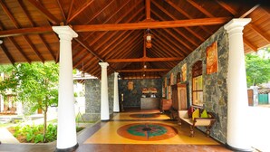A covered area with a stone wall, wooden columns, and a reception desk. - Peacock Wild Yala (Thissamaharama)