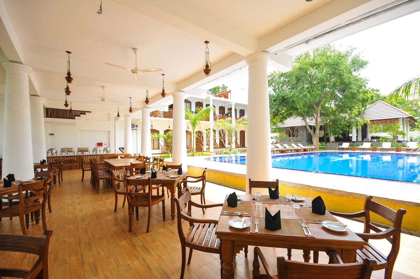 A restaurant with wooden tables and chairs, a pool view, and ceiling fans.