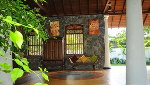 A traditional room with a stone wall, wooden furniture, and a bench with cushions. - Peacock Wild Yala (Thissamaharama)