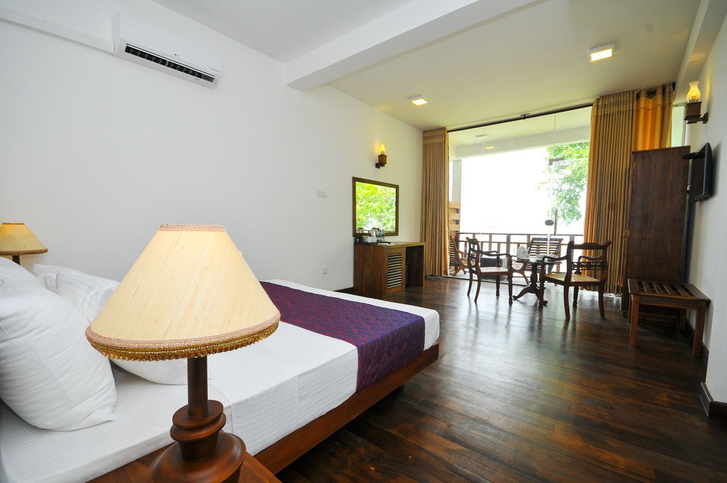 A hotel room with a bed, a table with chairs, a TV, and a window with curtains.