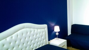 Een slaapkamer met een bekleed hoofdeinde, een witte nachtkastje met een lamp, en een donkerblauwe bank.