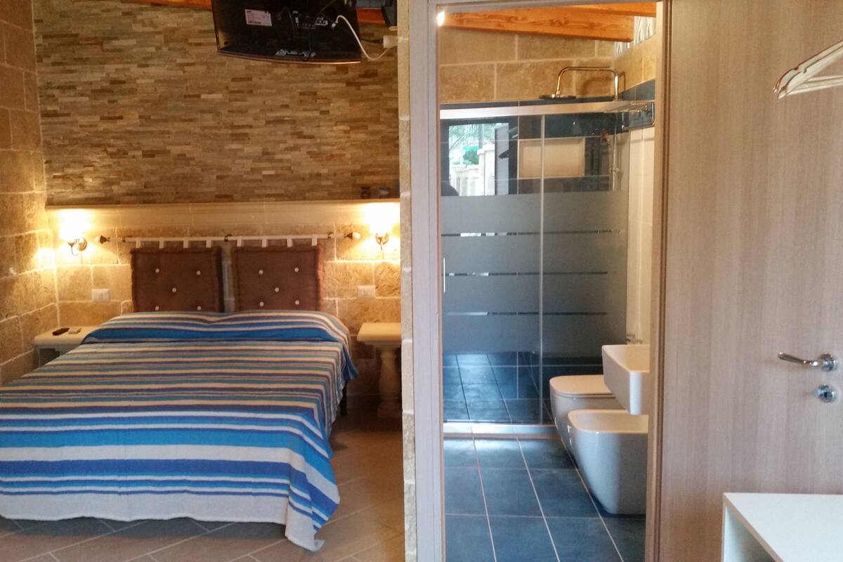 Une chambre à coucher comprenant un lit, une table de chevet, un mur en briques et une salle de bain avec des toilettes et un lavabo.