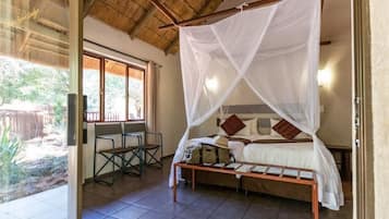 Una habitación con una cama bajo una mosquitera, una mesita y sillas.