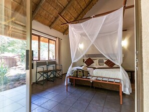 A room with a bed under a mosquito net, a small table, and chairs.