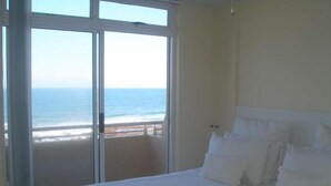 Un dormitorio con una cama grande, ropa de cama blanca y vistas al océano a través de un ventanal corredizo.