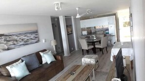 Una sala de estar moderna con un sofá marrón, una mesa de comedor con sillas y una cocina al fondo.
