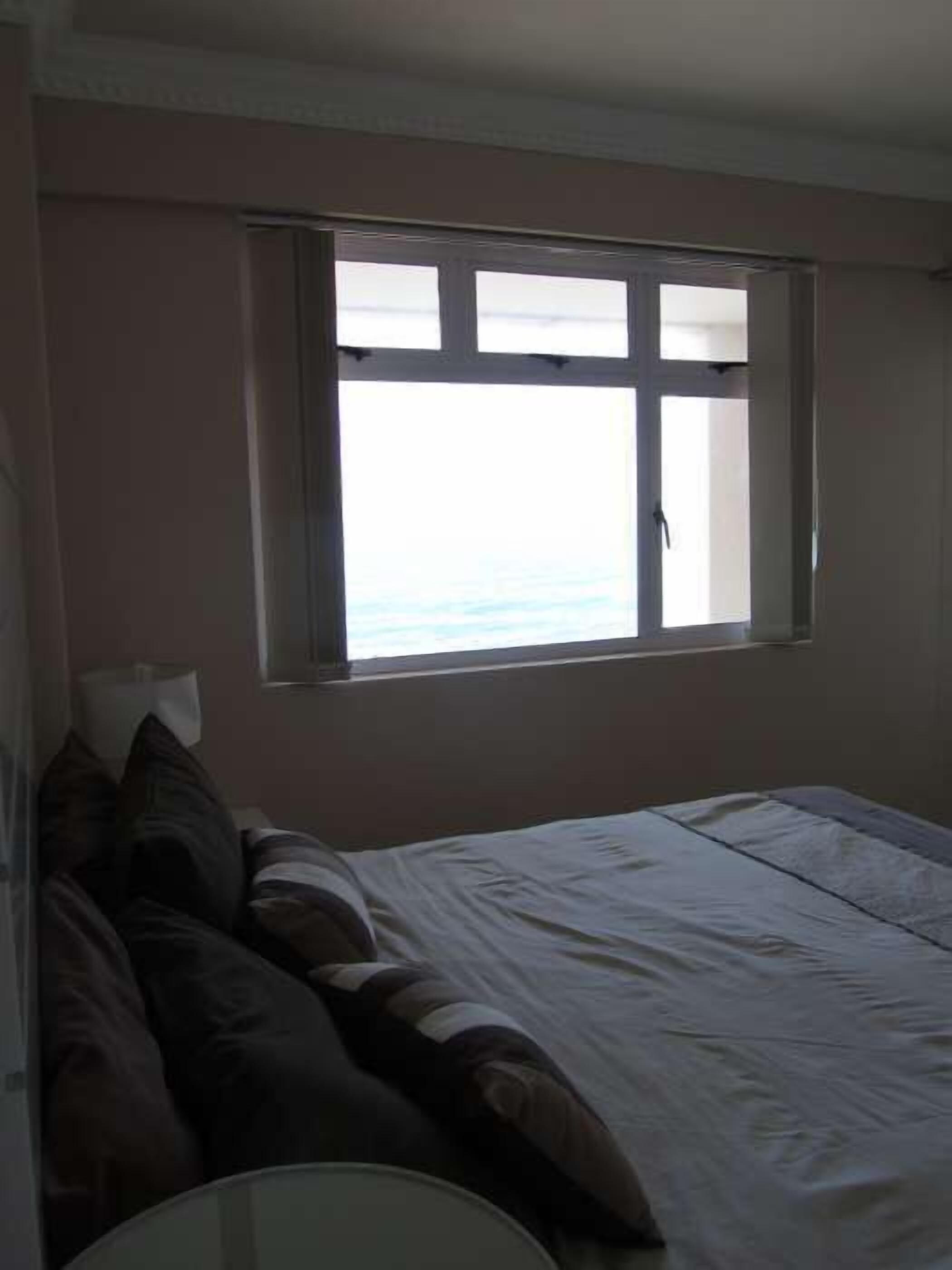 A bedroom with a bed, pillows, a window, and a lamp.