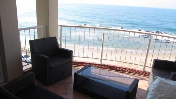 Un balcón con vista al océano, que incluye una silla, una mesita y un sofá.