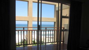 Una habitación con un ventanal grande con vista a la playa, una cama y una pequeña mesa.
