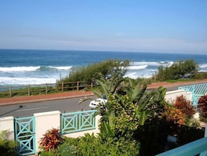 A coastal view with a road leading to a gated entrance, surrounded by lush greenery and a clear view of the ocean. - Waterfront (eMdloti)