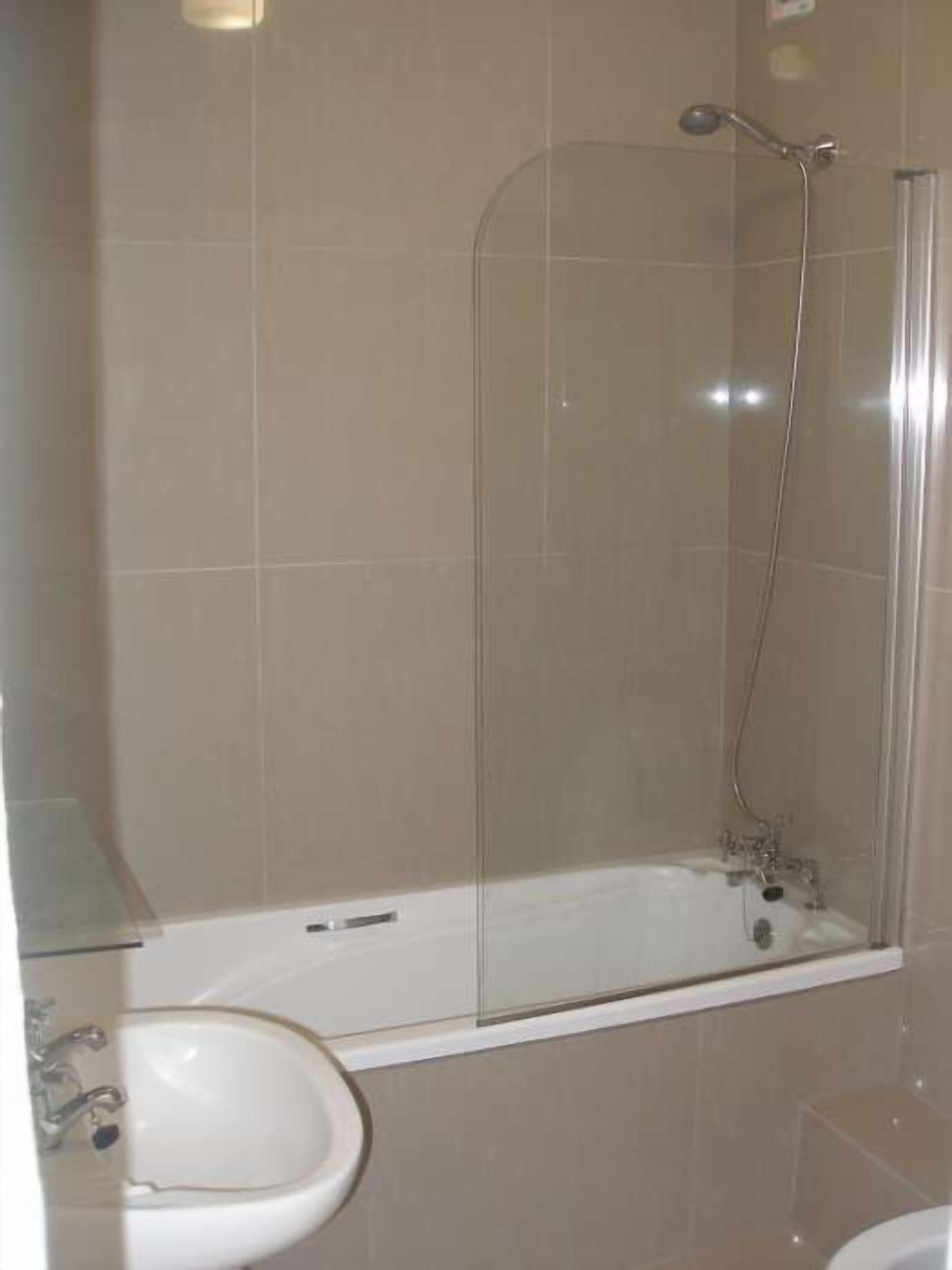 A bathroom with a glass-enclosed shower, a white sink, and a toilet.