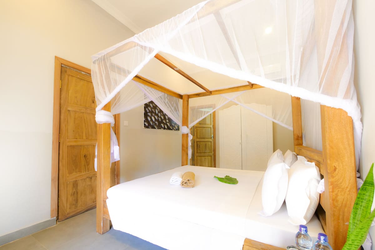 Uma cama com dossel, guarda-roupa de madeira e uma planta verde.