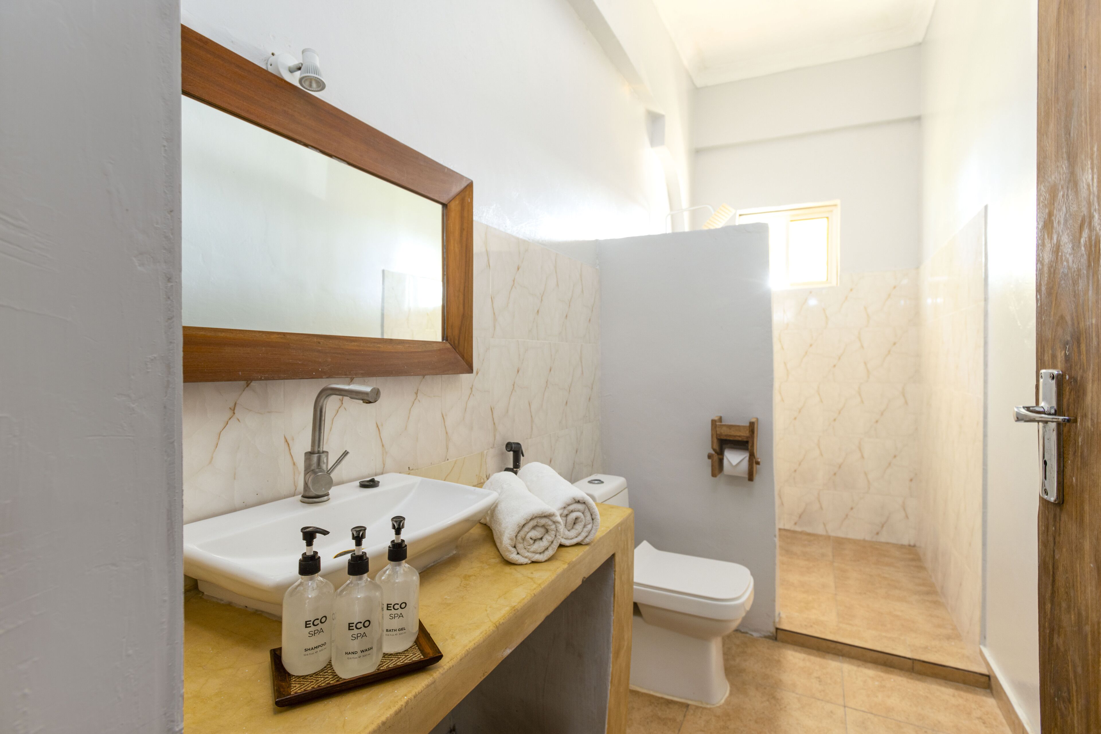A bathroom with a sink, mirror, and toilet. There are two bottles of shampoo and two towels on the sink.