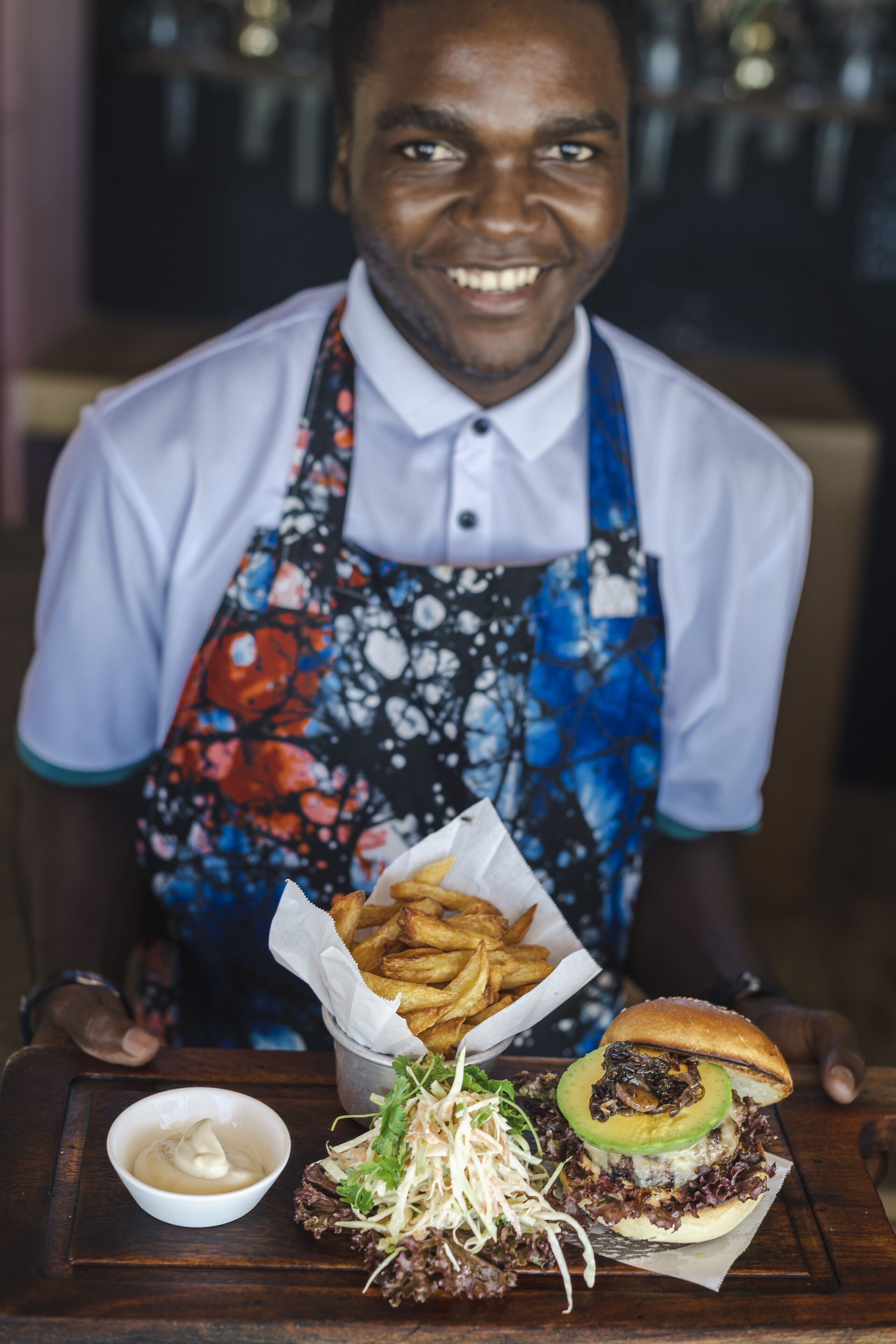Alguém servindo comida, incluindo um hambúrguer, batatas fritas e uma pequena tigela de molho.