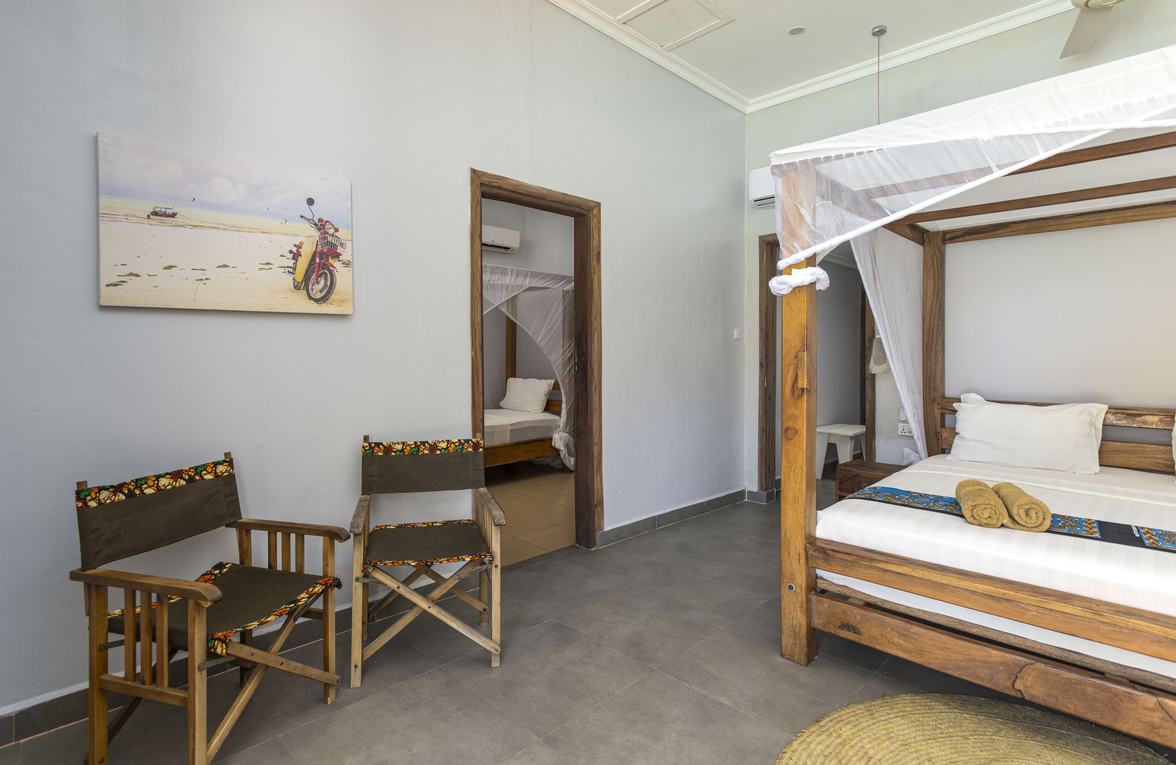A bedroom with a bed, a chair, a small table, and a painting of a motorcycle on the wall.