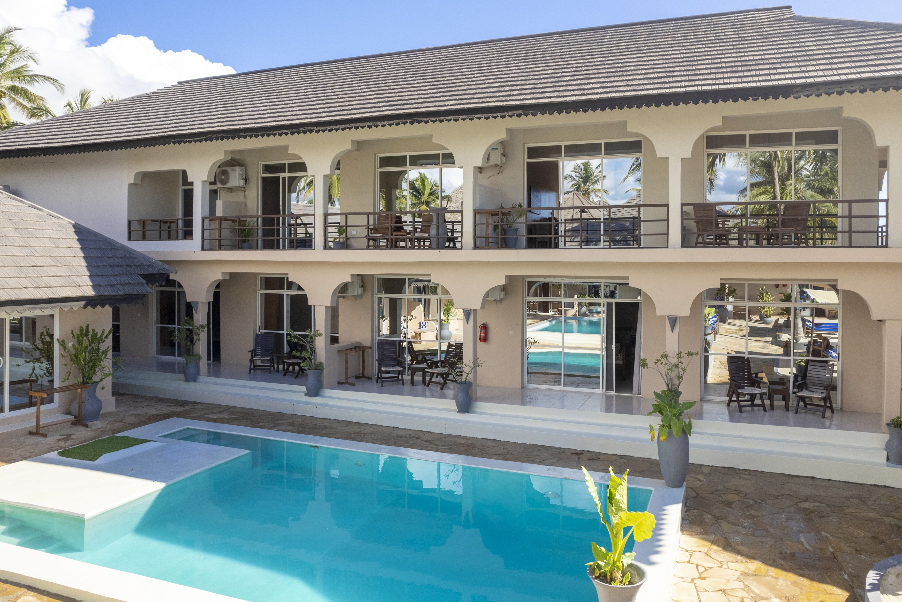 Ein Hotel mit zwei Etagen, einem Swimmingpool, Sitzgelegenheiten im Freien und Blick auf den Pool.
