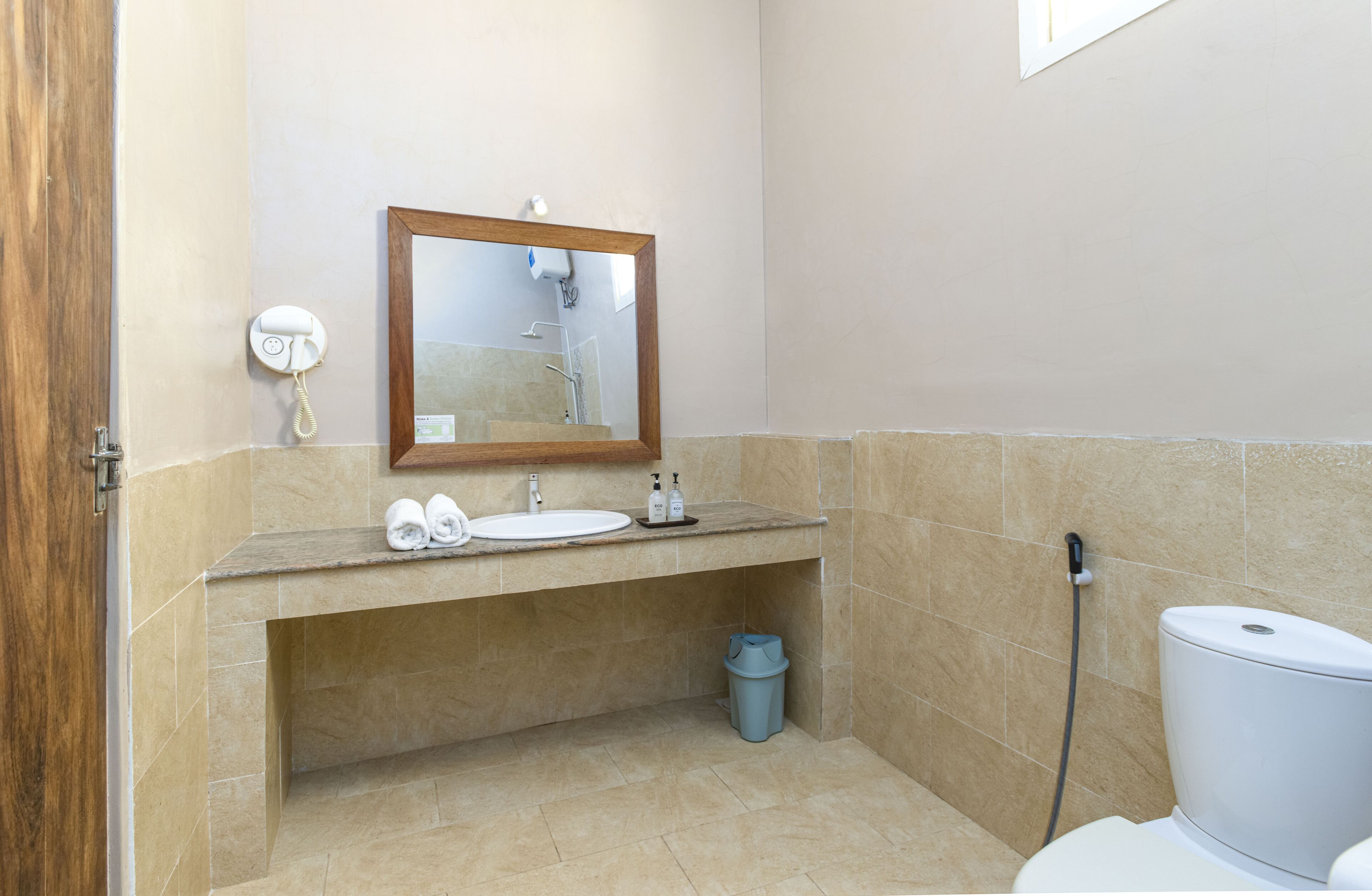 A bathroom with a sink, mirror, toilet, and a trash bin.
