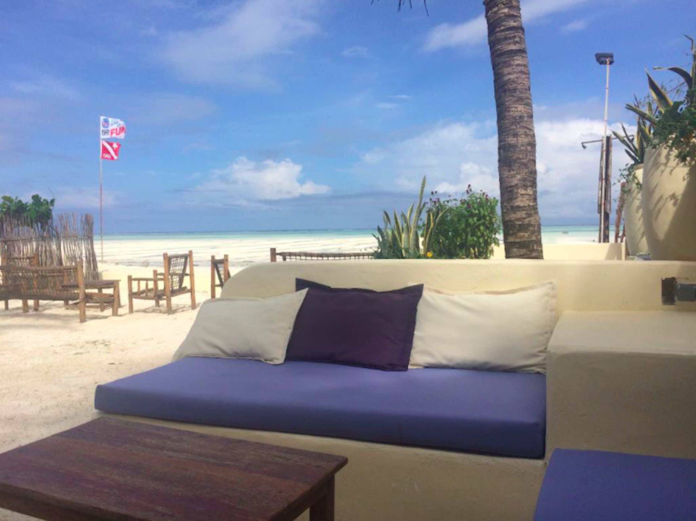 Un salón junto a la playa con sofá y mesa de madera, con vista a una playa arenosa y el océano.