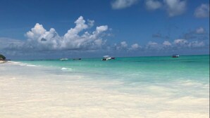 A beach with clear turquoise water, white sand, and a few boats in the distance. - Paje Beach Apartments & Hotel (Paje)