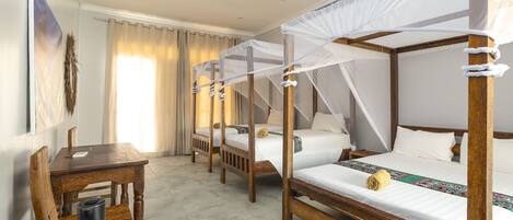 Una habitación con cuatro camas de madera, cada una con dosel, un ventilador de techo y una mesa con una cesta de aperitivos.