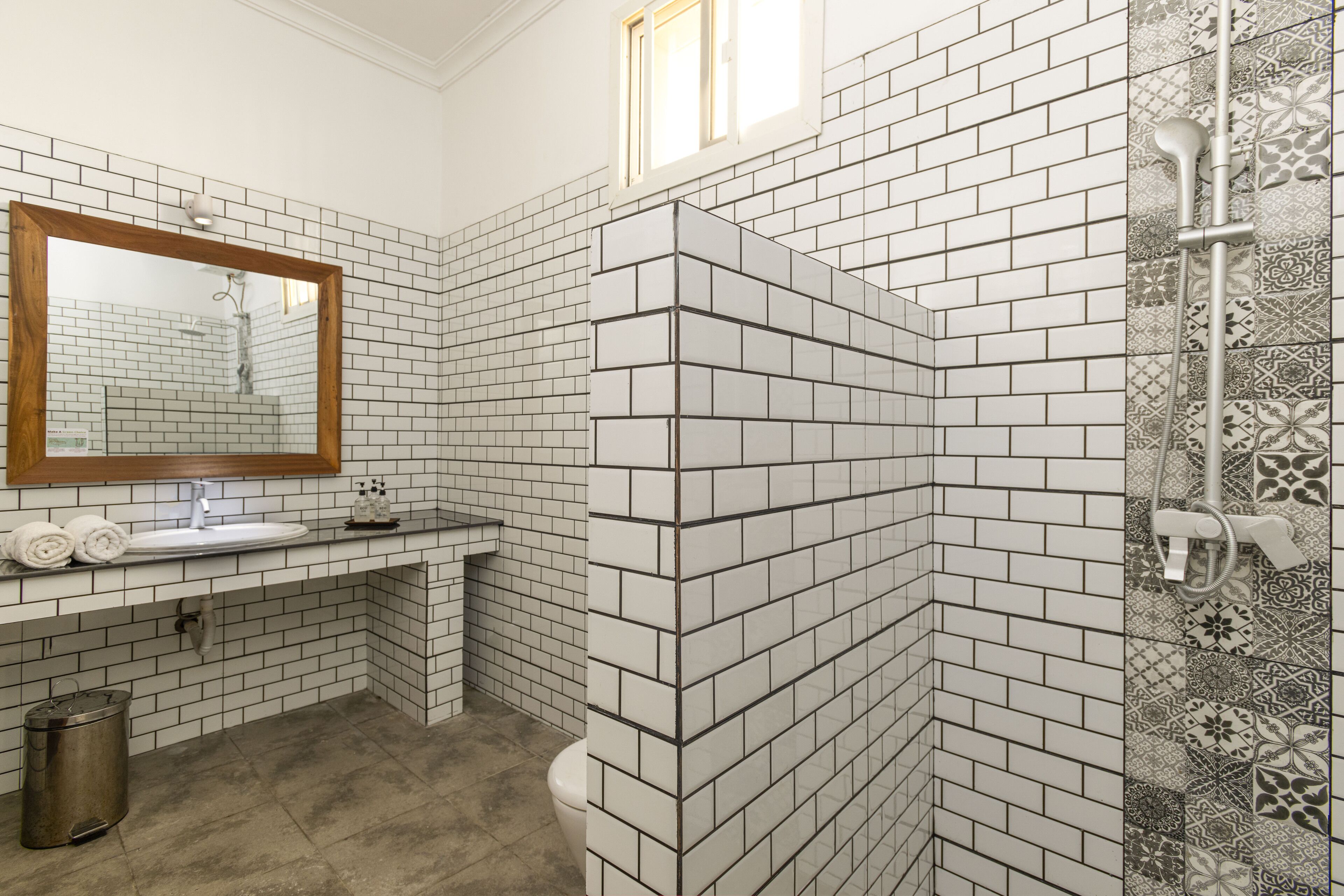 Un baño con paredes de azulejos blancos y negros, un espejo con marco de madera, un lavamanos y una zona de ducha.