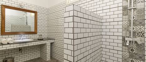 Un baño con paredes de azulejos blancos y negros, un espejo con marco de madera, un lavamanos y una zona de ducha.