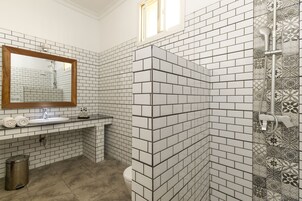A bathroom with white and black tiled walls, a wooden-framed mirror, a sink, and a shower area.
