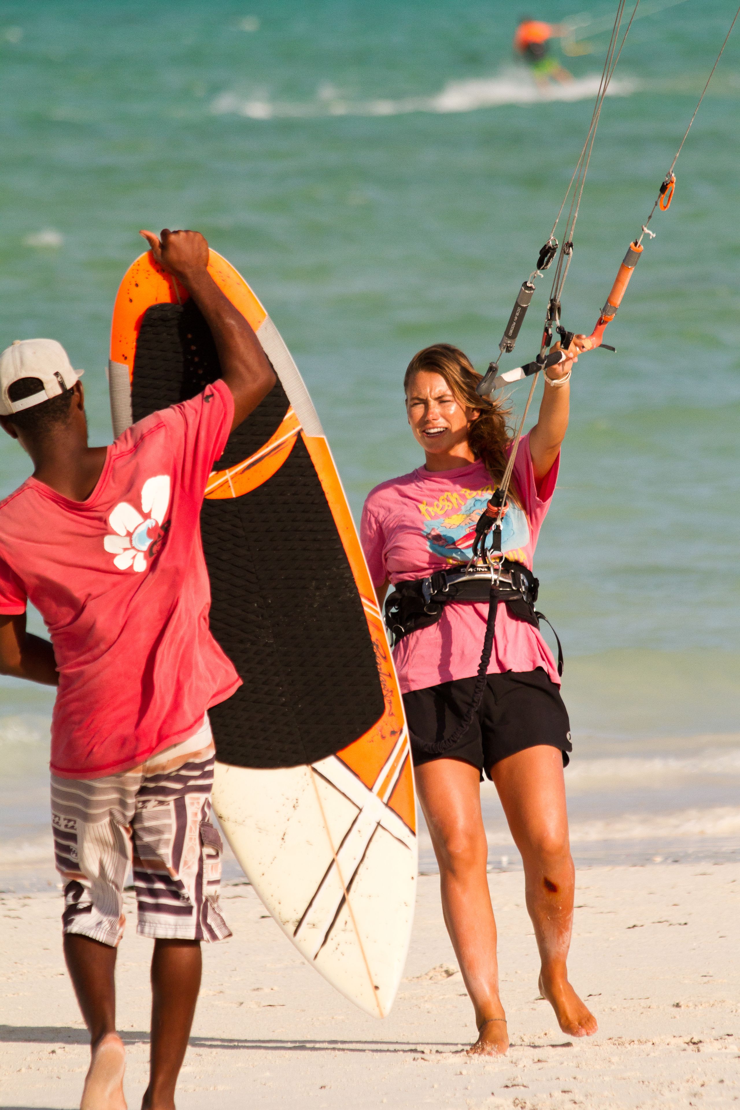 Two people walking on a beach with a surfboard and a kiteboard.