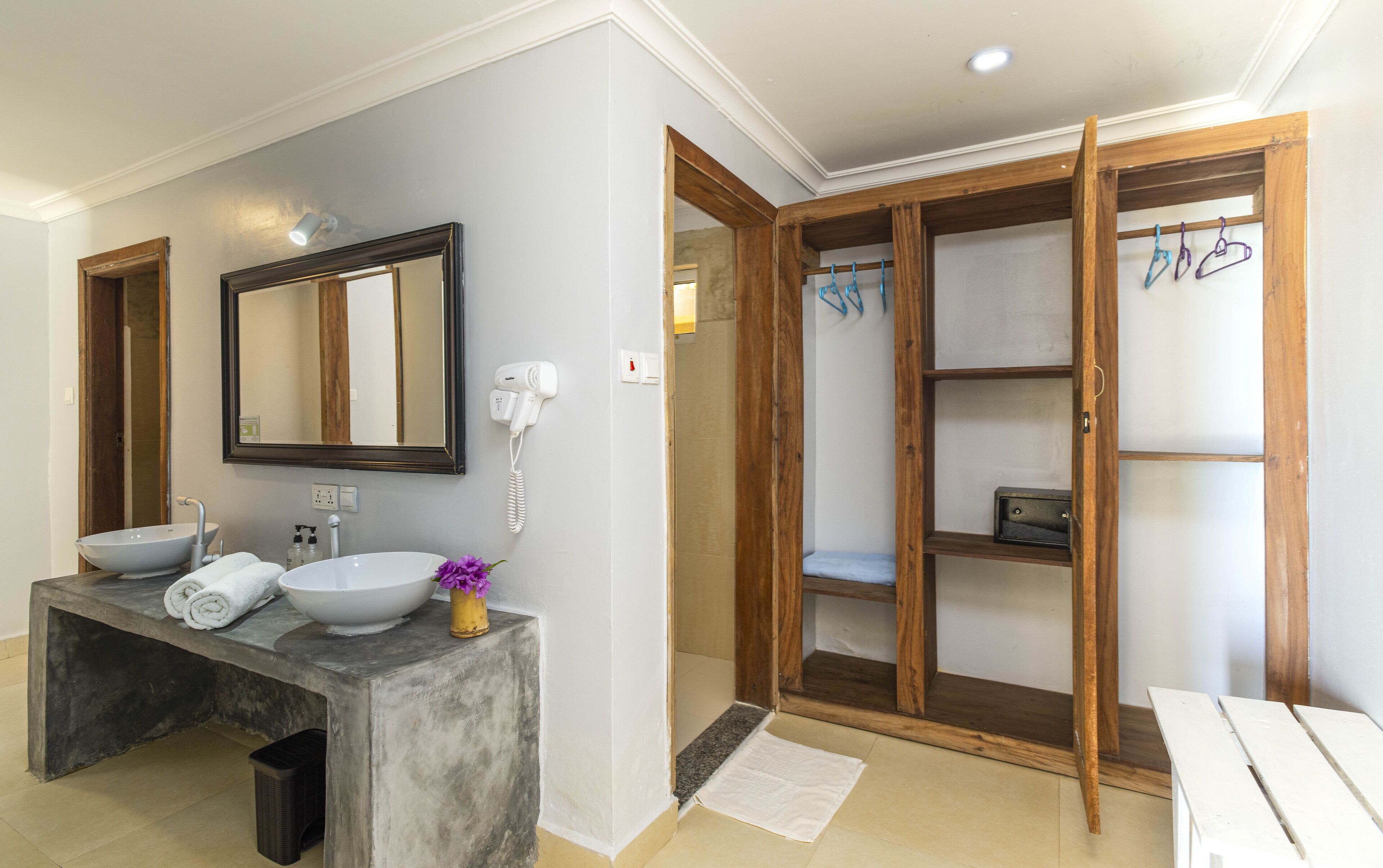 A bathroom with a large mirror, two sinks, a hairdryer, and a wooden wardrobe with a towel rack.