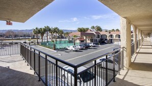 A balcony with a view of a parking lot, palm trees, and a building with a red roof. - Hotel Palmdale - Antelope Valley (Palmdale)