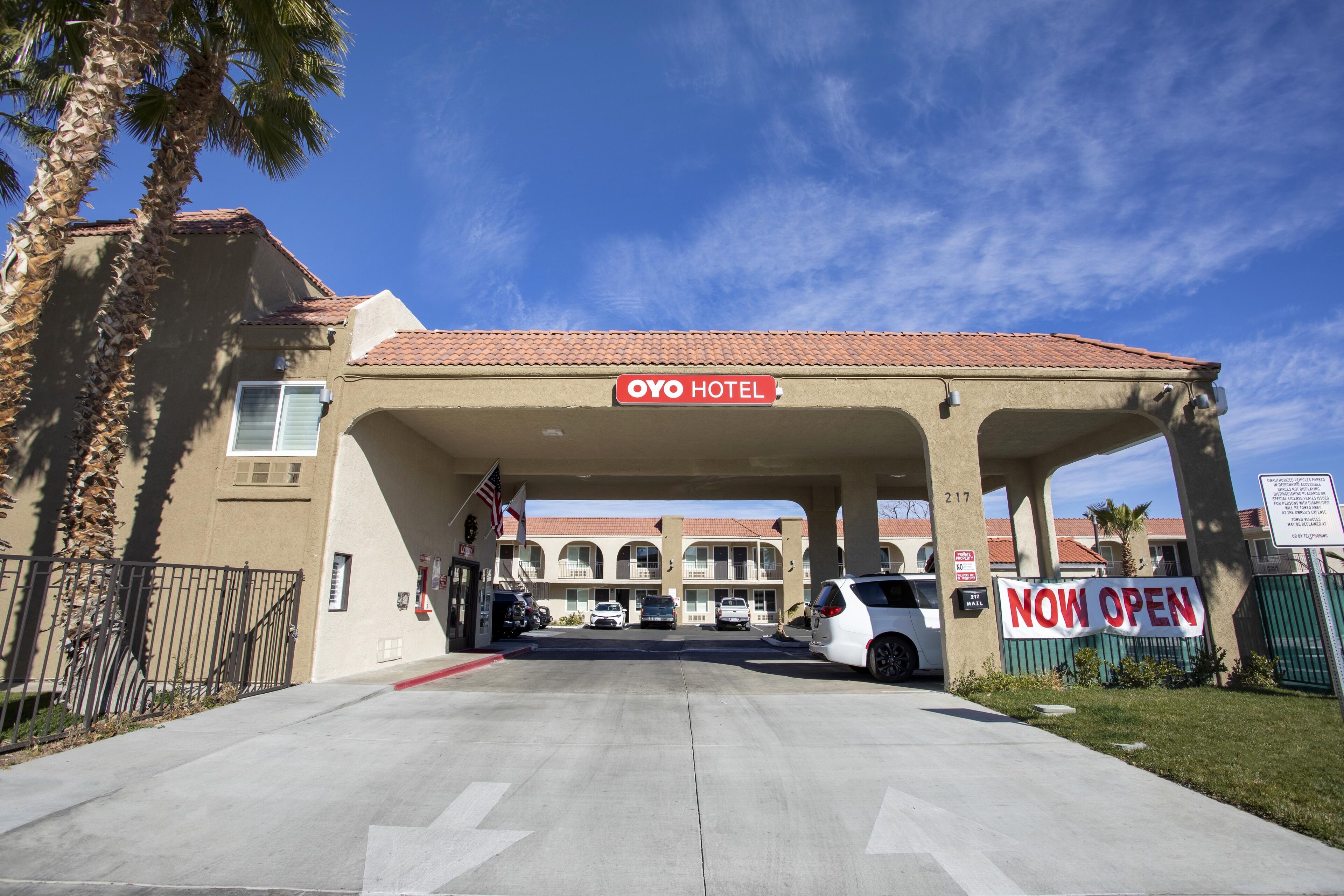The OYO Hotel entrance with a 'NOW OPEN' sign, a covered parking area, and a clear sky.