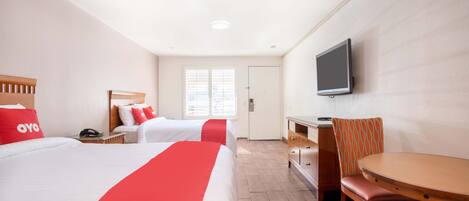 A hotel room with two beds, a desk, a chair, a TV, and a window.