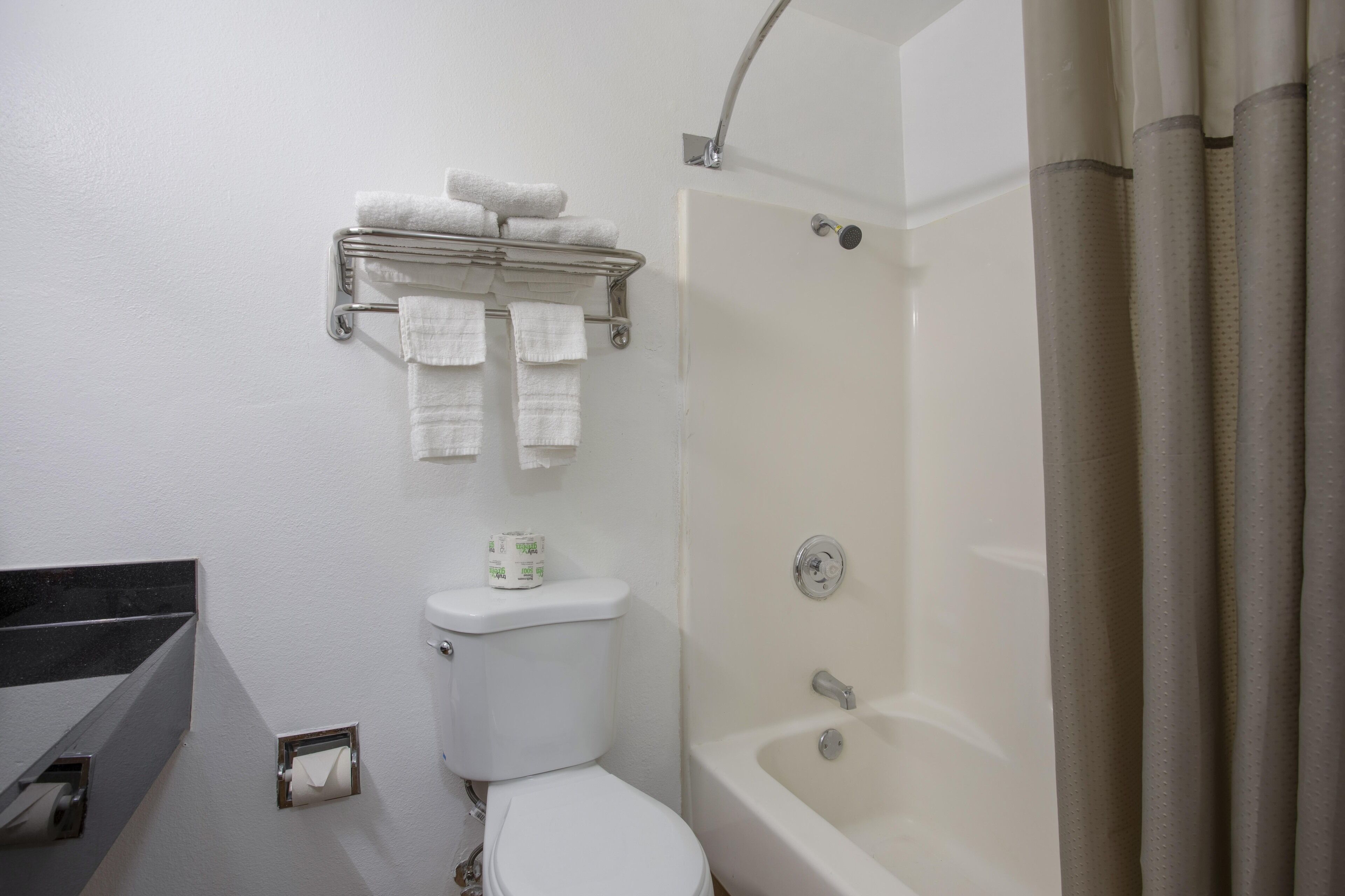 A bathroom with a toilet, a shower, and a towel rack with towels.