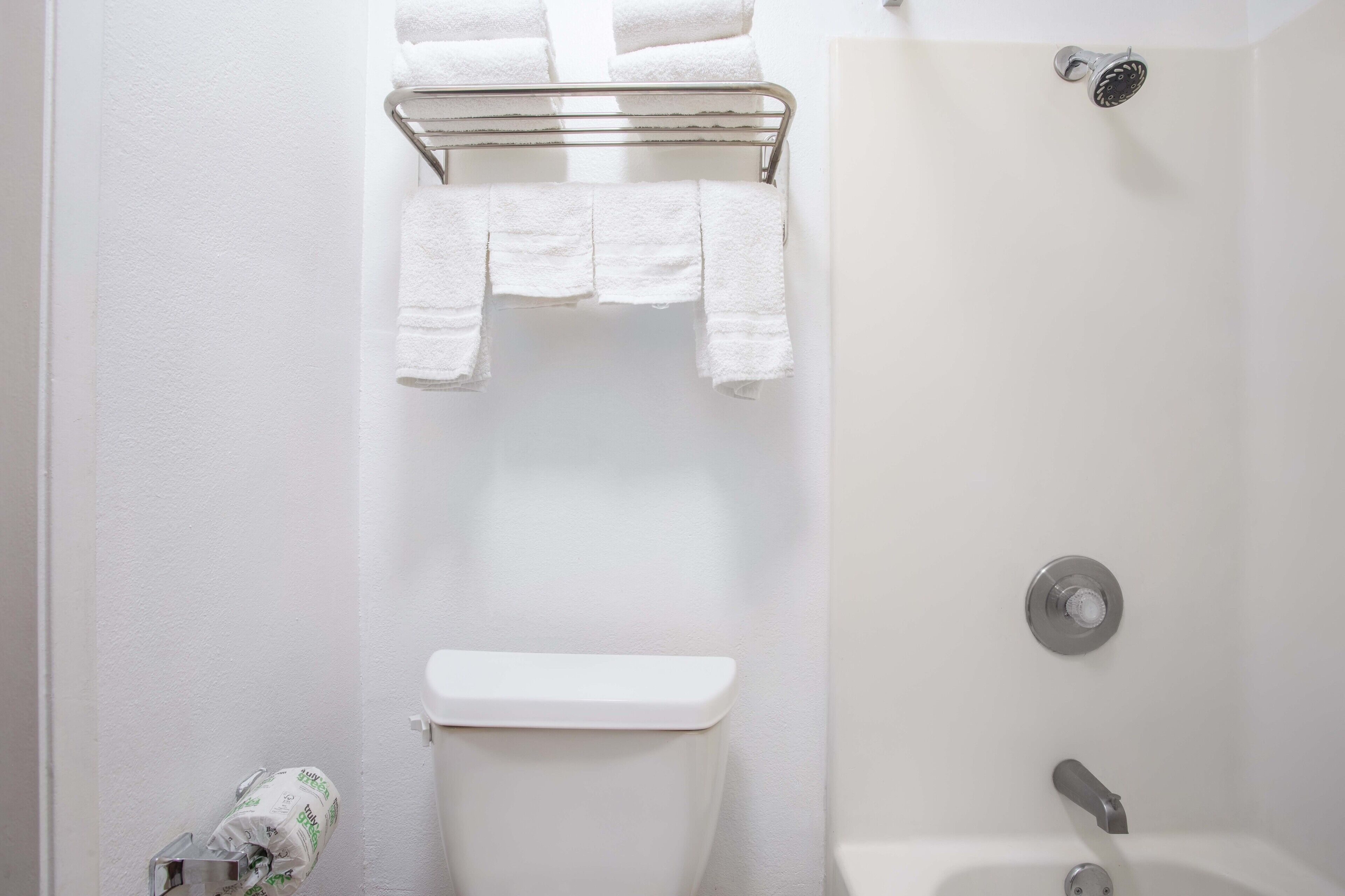 A bathroom with a toilet, a shower, and a towel rack with towels.