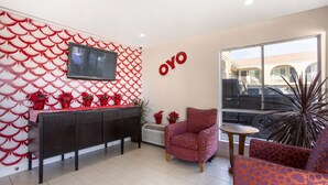 A modern hotel lobby with a red and white patterned wall, a flat-screen TV, a reception desk, and seating areas. - Hotel Palmdale - Antelope Valley (Palmdale)