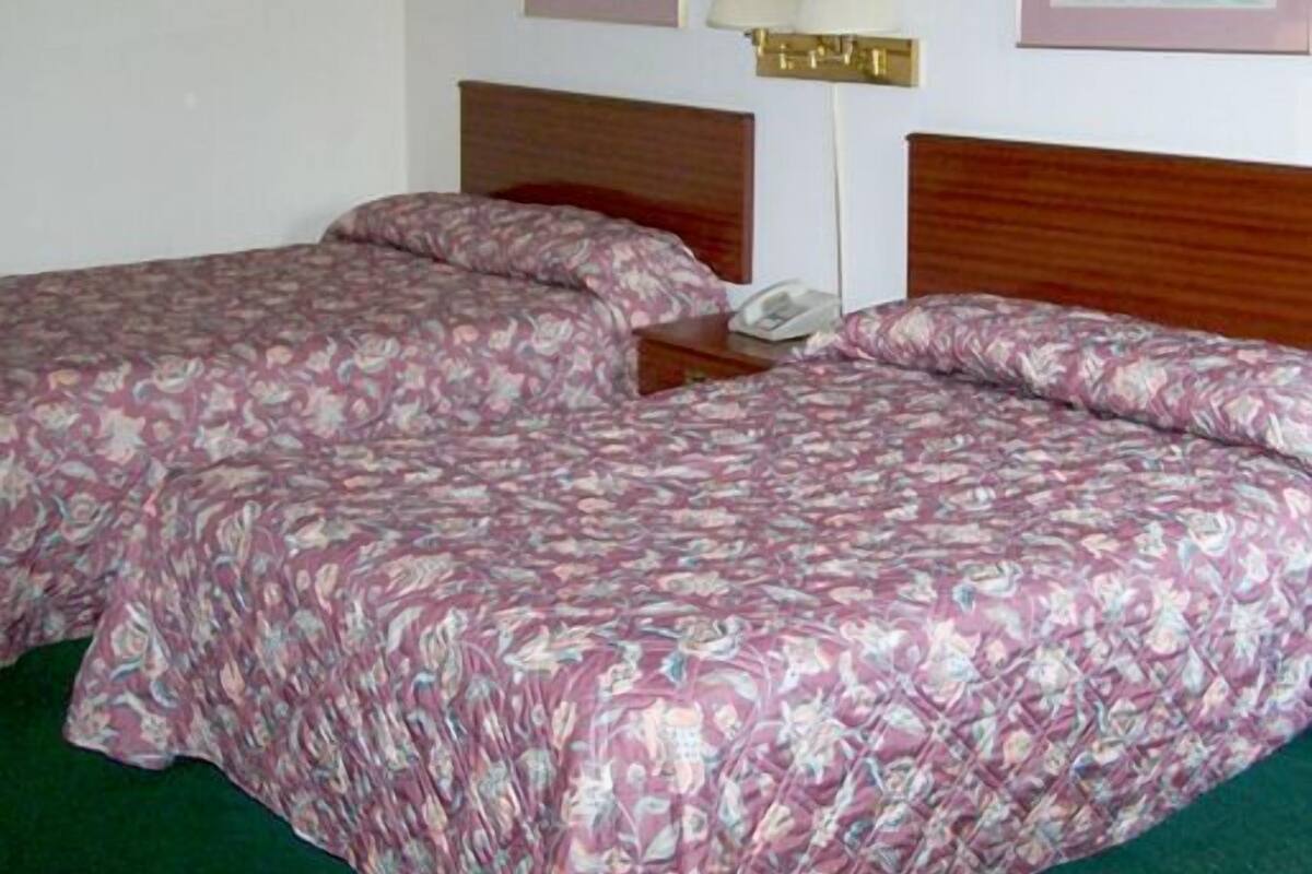 Une chambre d’hôtel avec deux lits, une table de chevet, une lampe et deux tableaux encadrés au mur.