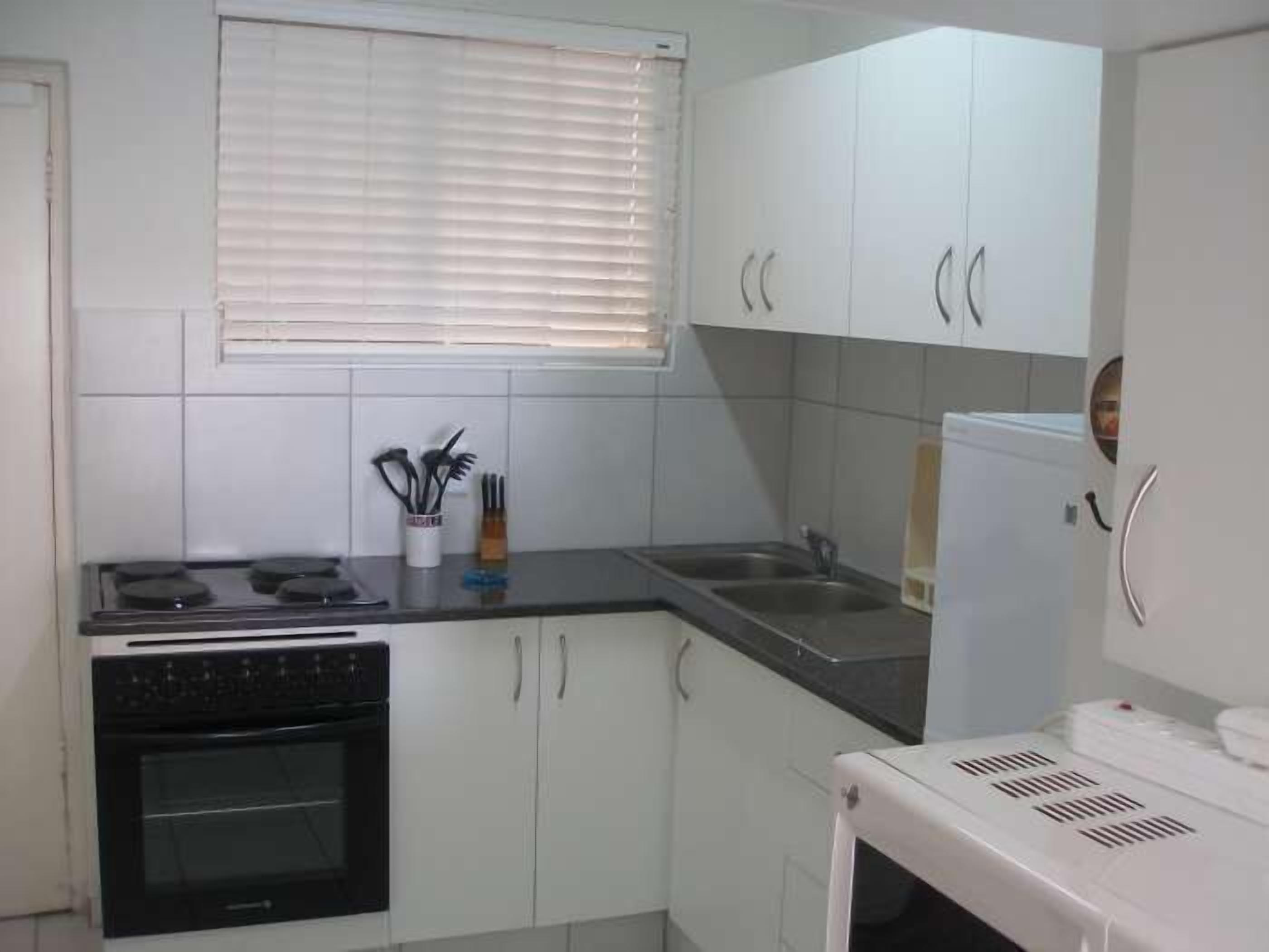 A compact kitchen with white cabinets, a built-in oven, a microwave, and a sink.