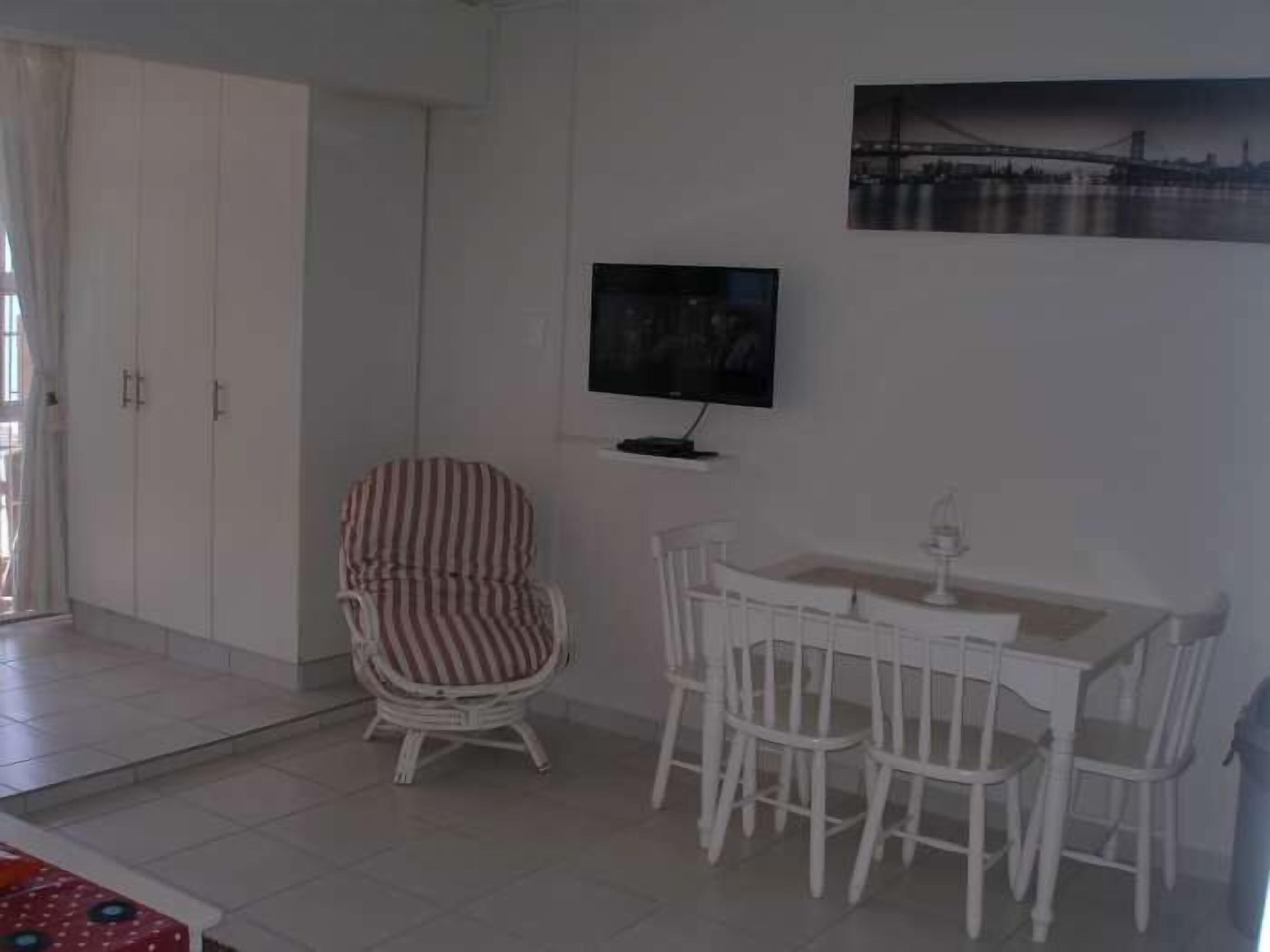 Une pièce comprenant une table à manger et des chaises, une chaise à rayures, un téléviseur fixé au mur et une armoire.